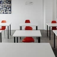 Heller Klassenraum mit weißen Tischen und roten Stühlen